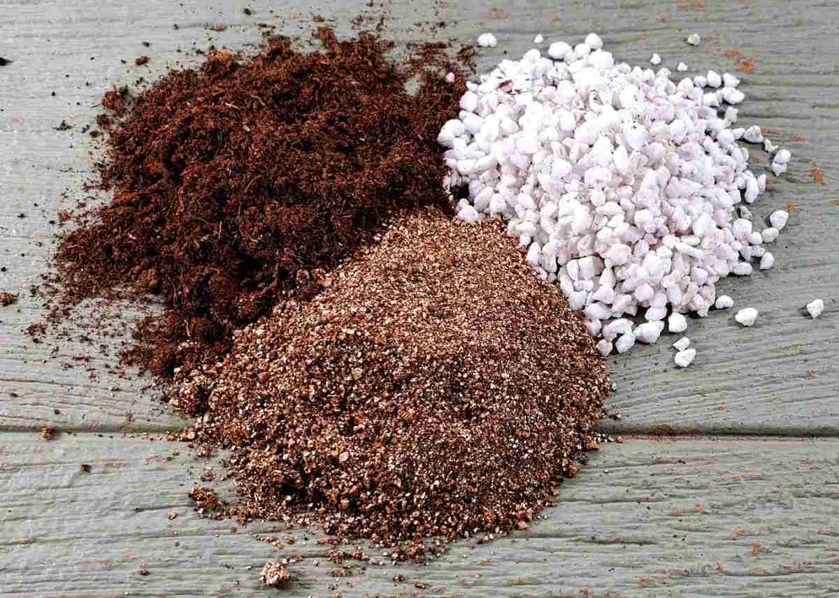 Peat moss, perlite and vermiculite in small piles on a wooden counter.